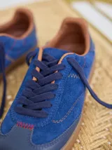 Championes de cuero color tostado con detalles metalizados y pespuntes decorativos en verde y azul. Cuentan con cordones marrones y suela de goma texturizada.