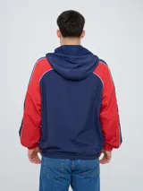 Campera deportiva Umbro del Club Nacional de Football, modelo Venti, para hombre. Diseño en color blanco con mangas azules y detalles de líneas rojas. Cuenta con capucha con cordón ajustable, cierre frontal y bolsillos. Presenta el logo de Umbro y el escudo del club bordados en el pecho.