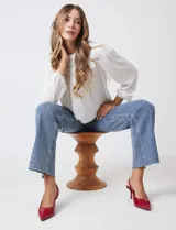 Blusa azul de gasa con pliegues en la parte delantera y detalles de encaje calado. Cuello alto fruncido y mangas largas con puños elastizados. Espalda lisa con abertura tipo gota y botón.