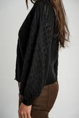 Cardigan negro de algodón con cuello en V, cierre frontal de botones y mangas largas con textura calada. Presenta puños y ruedo acanalados.