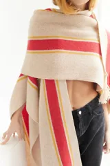 Ruana artesanal de tejido de punto, color beige con franjas horizontales gruesas rojas y finas amarillas. Posee flecos en el borde inferior.