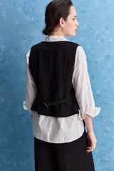 Chaleco negro con escote en V, cierre frontal con botones y bolsillos ribeteados simulados.