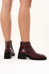 Bota corta de cuero color bordó, con punta cuadrada, taco bloque y plataforma. Presenta cierre lateral interno y detalle de ribete en la capellada.