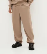 Pantalón baggy masculino de corte holgado, color beige, confeccionado en algodón con felpa. Posee cintura elástica con cordón ajustable, bolsillos delanteros y bajo con regulador por elástico.