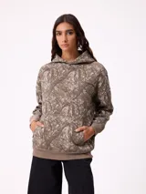 Canguro con capucha de corte holgado, estampado con diseño de ramas en tonos marrones y beige. Presenta bolsillo frontal tipo canguro, puños y ruedo en tejido rib elástico, y logo de la marca bordado en el pecho.