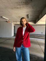 Blazer rojo con solapas, cierre con un botón dorado y escudo bordado en el bolsillo.