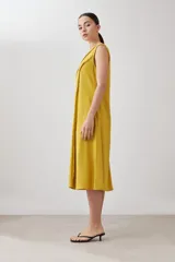 Vestido midi acampanado color mostaza, sin mangas, confeccionado en lino con detalle desflecado en los bordes. Incluye una bufanda del mismo material y color.