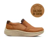 Zapato casual tipo slip-on de cuero color tostado con textura granulada. Presenta una suela de plataforma ergonómica en color beige con diseño texturizado y detalles en tejido marrón en el cuello y lengüeta.