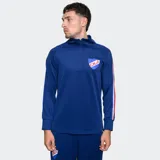 Buzo deportivo de entrenamiento del Club Nacional de Football, color azul, con cuello alto y cierre frontal parcial. Presenta mangas largas con franjas laterales en colores rojo, blanco y azul, y el escudo del club en el pecho.