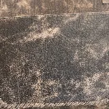 Cartera tipo tote de cuero marrón con costuras artesanales visibles, bolsillo frontal con el logo grabado, asas de hombro y detalles de flecos colgantes.