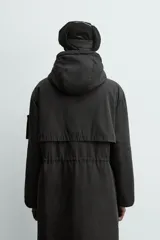 Parka técnica de corte relajado con acabado repelente al agua. Presenta cuello subido con capucha ajustable, cierre frontal con cremallera oculta por solapa con botones y cintura ajustable con cordón. Incluye múltiples bolsillos frontales con solapa, un bolsillo con cremallera en la manga y puños con interior en rib. El diseño cuenta con interior acolchado y aberturas laterales con cremallera en el bajo.