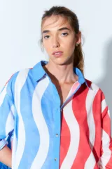 Túnica tipo vestido camisero corto con estampado de rayas onduladas verticales en colores rojo, blanco y azul. Tiene cuello camisero, cierre frontal con botones y mangas largas con puños abotonados.