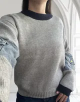 Sweater gris de punto con cuello redondo azul marino y mangas largas con apliques de denim y bolsillos con botón.