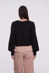 Sweater negro de tejido de punto con diseño cruzado en el frente, escote en V profundo y mangas largas con puños ajustados.