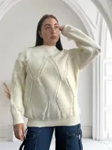 Sweater blanco de tejido de punto con cuello redondo y mangas largas. Presenta un diseño con rombos y flecos.