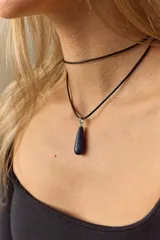Gargantilla de cuero negro con dije de piedra blanca en forma de lágrima con engarce dorado.