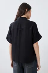Camisa negra de manga corta con cuello clásico y cierre frontal con botones.