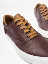 Championes urbanos de cuero sintético en tono bordó, con detalles perforados en los laterales y puntera lisa. Presenta cordones planos en color tostado, cuello acolchado y suela de goma blanca con textura en la puntera.