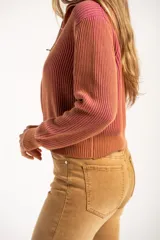 Campera tejida de algodón con diseño acanalado, cuello alto y cierre frontal completo. Presenta un patrón bicolor en tonos terracota y rosado, con puños y cintura elásticos.