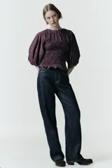 Blusa de color bordó con estampado de lunares claros, confeccionada con cuerpo en nido de abeja elástico, cuello redondo y mangas abullonadas por debajo del codo.
