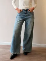 Pantalón de jean con corte wide leg y tiro medio-alto. Presenta un lavado gris azulado desgastado con acabado vintage y ruedo desflecado.