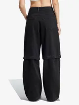 Pantalón de denim negro de corte ancho con tres tiras blancas verticales en los laterales y logo de Adidas.