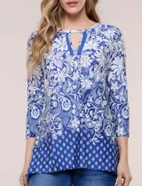 Blusa azul y blanca con estampado floral y geométrico, de calce suelto, con escote redondo, abertura tipo keyhole en el pecho, mangas tres cuartos y ruedo amplio con silueta evasé.