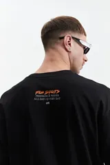 Remera negra de manga corta con corte oversize y cuello redondo. Presenta un estampado pequeño en la espalda con texto en naranja y blanco que dice "Free Spirits Freedom & Waves All Day / Every Day".