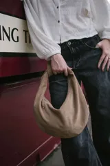 Cartera tipo hobo de gamuza marrón, diseño minimalista sin herrajes y cierre superior.