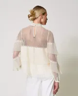 Blusa de tul point d'esprit color marfil, con cuello alto, volantes plisados, inserciones de encaje, mangas largas con puño y botón, cierre de lágrima con botón y placa con el logotipo Oval T en la parte trasera. Incluye top a juego antitransparencia y corte holgado.