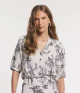 Camisa de viscolino Marfinno color beige con estampado de cocoteros en negro, cuello en V con escote hincapié y botones frontales negros. Mangas cortas con puños elásticos fruncidos.
