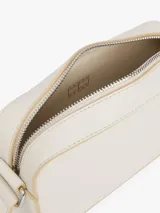 Cartera cruzada rectangular de color blanco roto, con ribetes y detalles en color beige claro. Presenta un parche rectangular con la insignia de Tommy Jeans en la parte frontal inferior derecha.