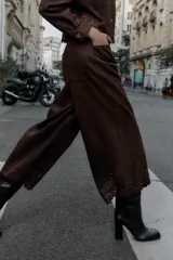 Pantalón culotte marrón de tiro alto con efecto ante, bolsillos delanteros y traseros, pernera ancha y corta. El bajo está troquelado con un diseño floral. Cierre frontal con cremallera y botón.