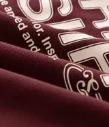 Remera de punto color bordó con ribetes blancos en los hombros y cuello polo, de corte holgado y manga corta. Cuenta con un diseño estampado en la espalda con texto en tonos claros.