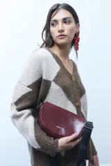 Riñonera de cuero vegano en color bordó con acabado brillante y efecto arrugado. Cuenta con dos compartimentos con cierre y correa ajustable de cinta negra.