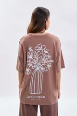 Remera de manga corta con corte oversize, color marrón, con estampa lineal blanca en la espalda que representa un florero con flores y el texto Jardin Fleuri.