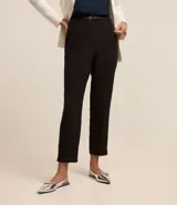 Pantalón carrot negro de sastrería, con bolsillos, pliegues y cinturón fino de cuero sintético.