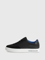 Zapatillas urbanas Calvin Klein con diseño de corte bajo. Presentan una combinación de materiales en la capellada, incluyendo paneles de nailon, cuero y ante en color negro. Destacan por su suela de goma blanca con el logo de la marca estampado en el lateral, forro interior en color azul vibrante y cierre mediante cordones.