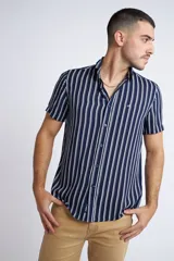 Camisa de manga corta con diseño a rayas verticales en color azul marino y blanco. Presenta cuello clásico, cartera abotonada frontal y logo bordado en el pecho. Posee un corte slim fit.