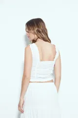 Top corto color marrón, con escote cuadrado y breteles anchos con volados. Presenta frunces horizontales en el torso y una hilera de botones nacarados en el centro frontal.