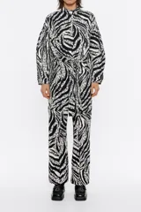 Mono largo estilo cargo con estampado animal print en blanco y negro. Tiene cuello con tira, manga larga con puño y botones de presión, suave fruncido en cintura y cinturón de tela con trabillas. Cierre frontal con botonadura de presión y bolsillos con pespuntes en el delantero.