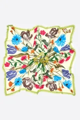Chal cuadrado confeccionado en modal con un diseño de estampado botánico floral en tonos azul, fucsia, amarillo y naranja sobre un fondo crema. Presenta bordes en color verde con acabado deshilachado.