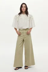 Blusa blanca con cuello mao, detalles de mini volados y bordados en el pecho y las mangas, con cierre frontal de botones y mangas largas abullonadas.