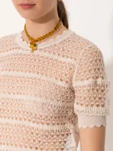Top de tejido crochet color beige, con cuello redondo y mangas cortas con terminación ondulada.