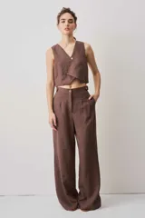 Pantalón de tiro alto color chocolate, con pinzas frontales que aportan caída suave y silueta amplia de pierna recta. Cierra con botón y bragueta, y suma un detalle de botón funcional en la cintura que le da un aire sastrero.