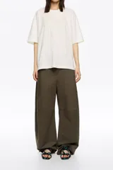 Pantalón de algodón color beige, de corte barrel ancho con tiro bajo. Presenta bolsillos en costuras delanteros y con vivo en la parte trasera. El bajo de la pierna tiene trabillas para ajustar el volumen.