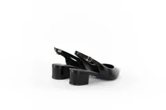 Zapato tipo slingback de charol negro con punta fina y taco cuadrado bajo de 4 cm. Presenta una tira ajustable en el talón con hebilla metálica.
