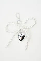 Llavero con diseño de lazo confeccionado en perlas sintéticas, con un dije colgante en forma de corazón metálico plateado y gancho mosquetón.