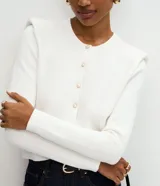 Cardigan de punto color blanco, de corte regular y ajuste al cuerpo. Presenta cuello redondo, mangas largas, cierre frontal con botones delicados y hombreras estructuradas que aportan volumen a la silueta.