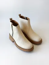 Bota corta de cuero vacuno con textura granulada, color crudo. Presenta cierre lateral metálico, suela track de goma en tono suela y tirador trasero.